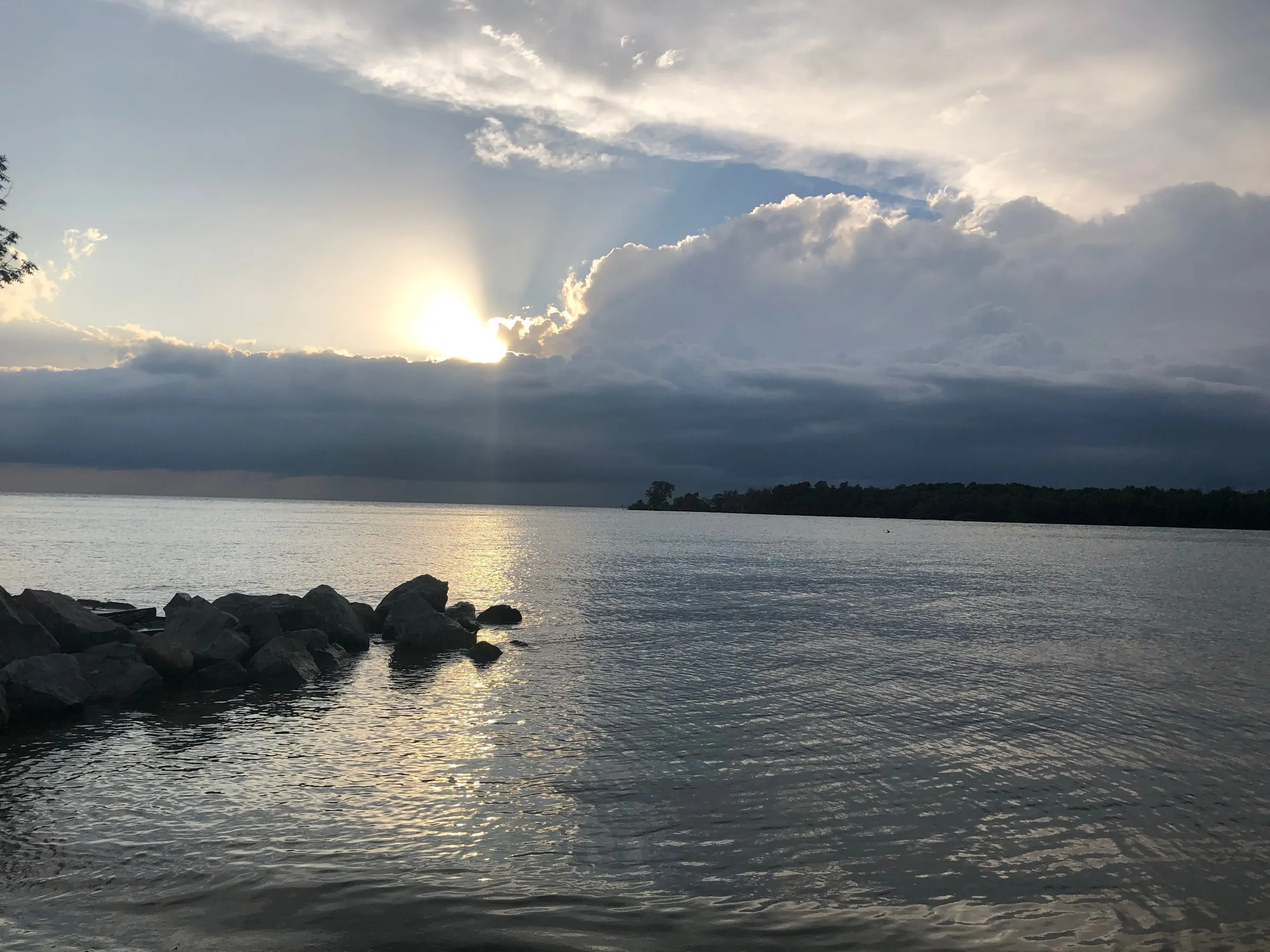 Sun breaking through a storm cloud over the lake and a rock breakwall