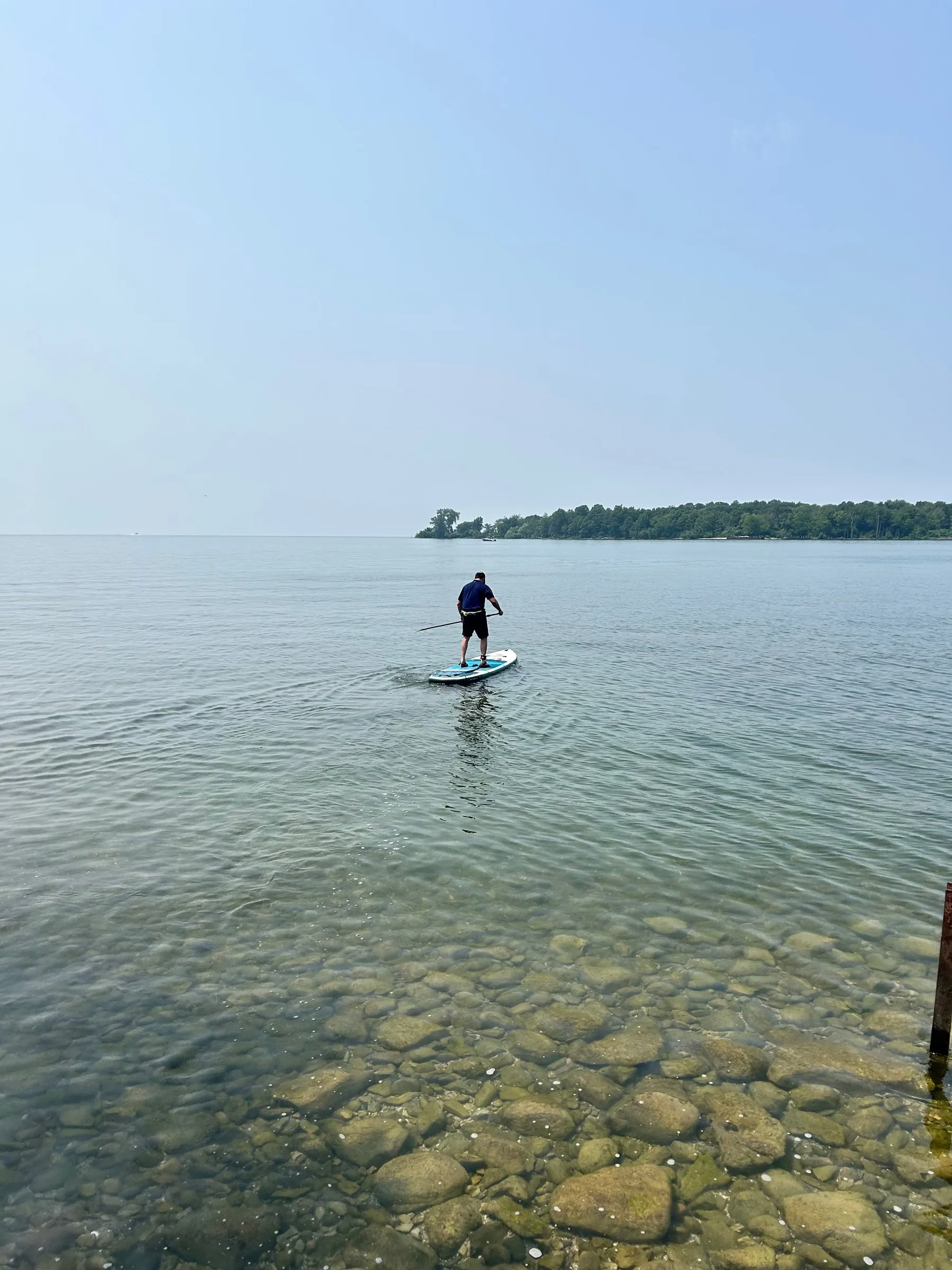 Water so clear the stones show, with a paddleboarder out in the distance