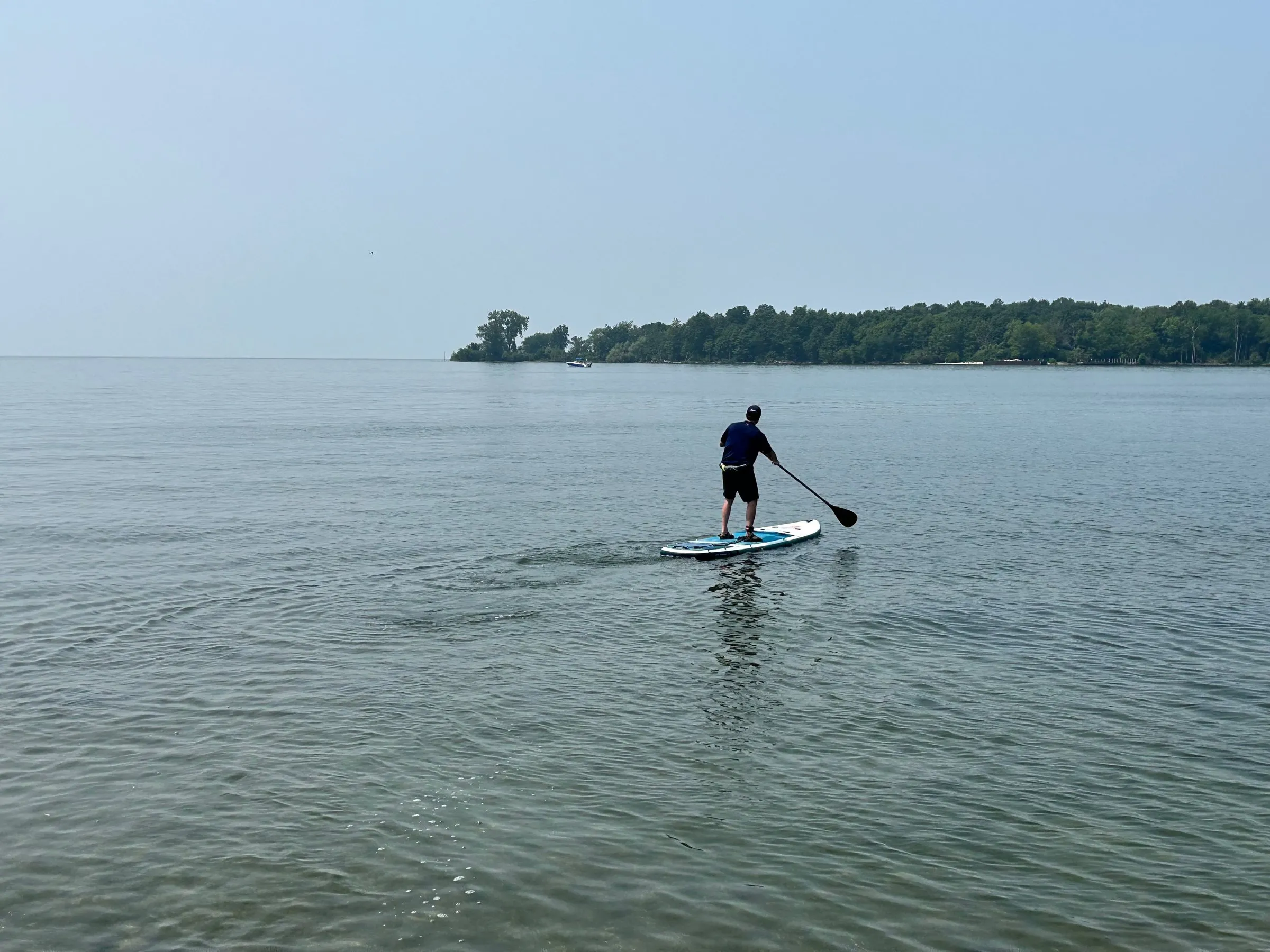 A paddleboarder heading out across calm water toward a low wooded island