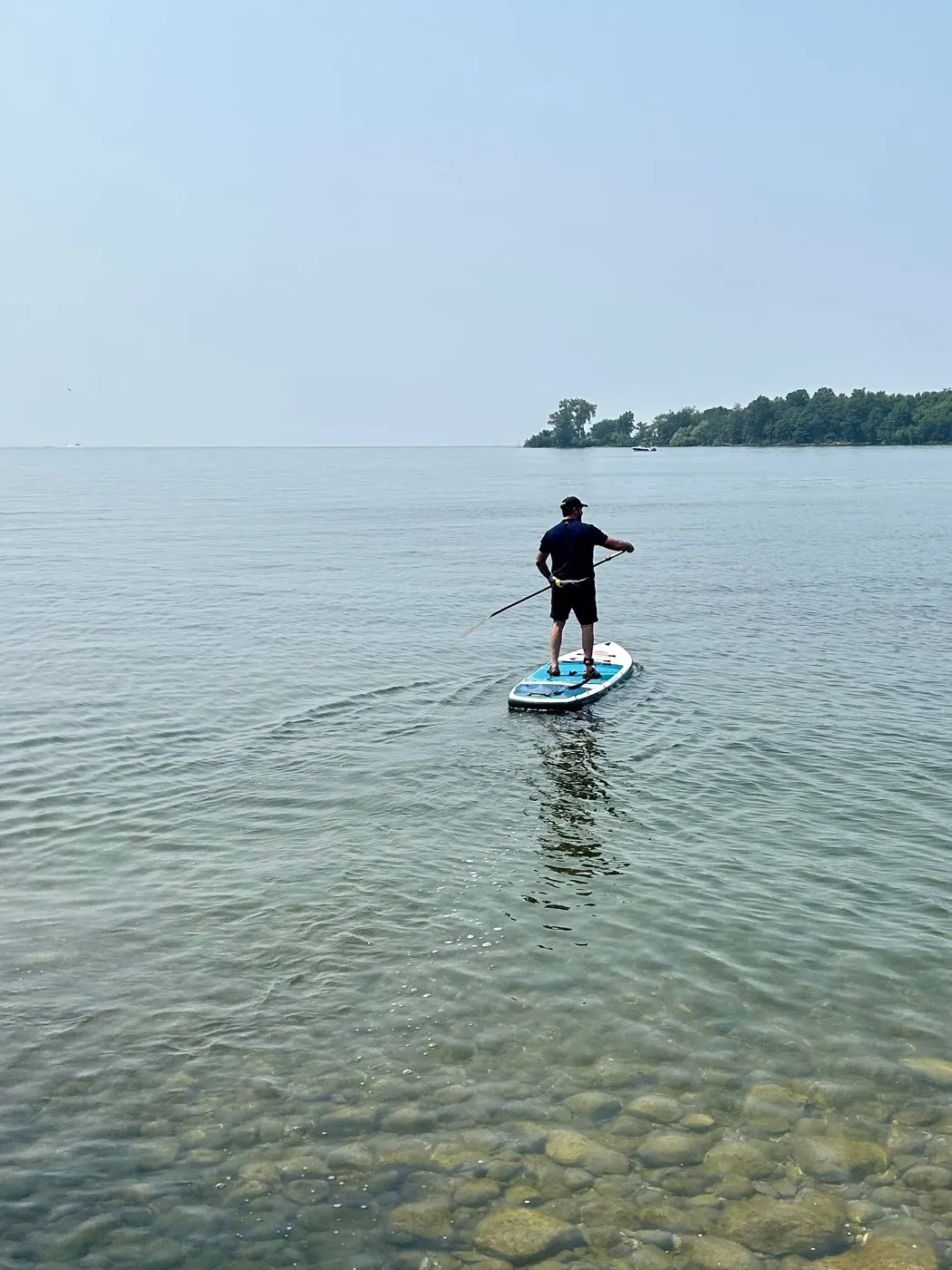 A paddleboarder standing on a board over clear water, an island ahead